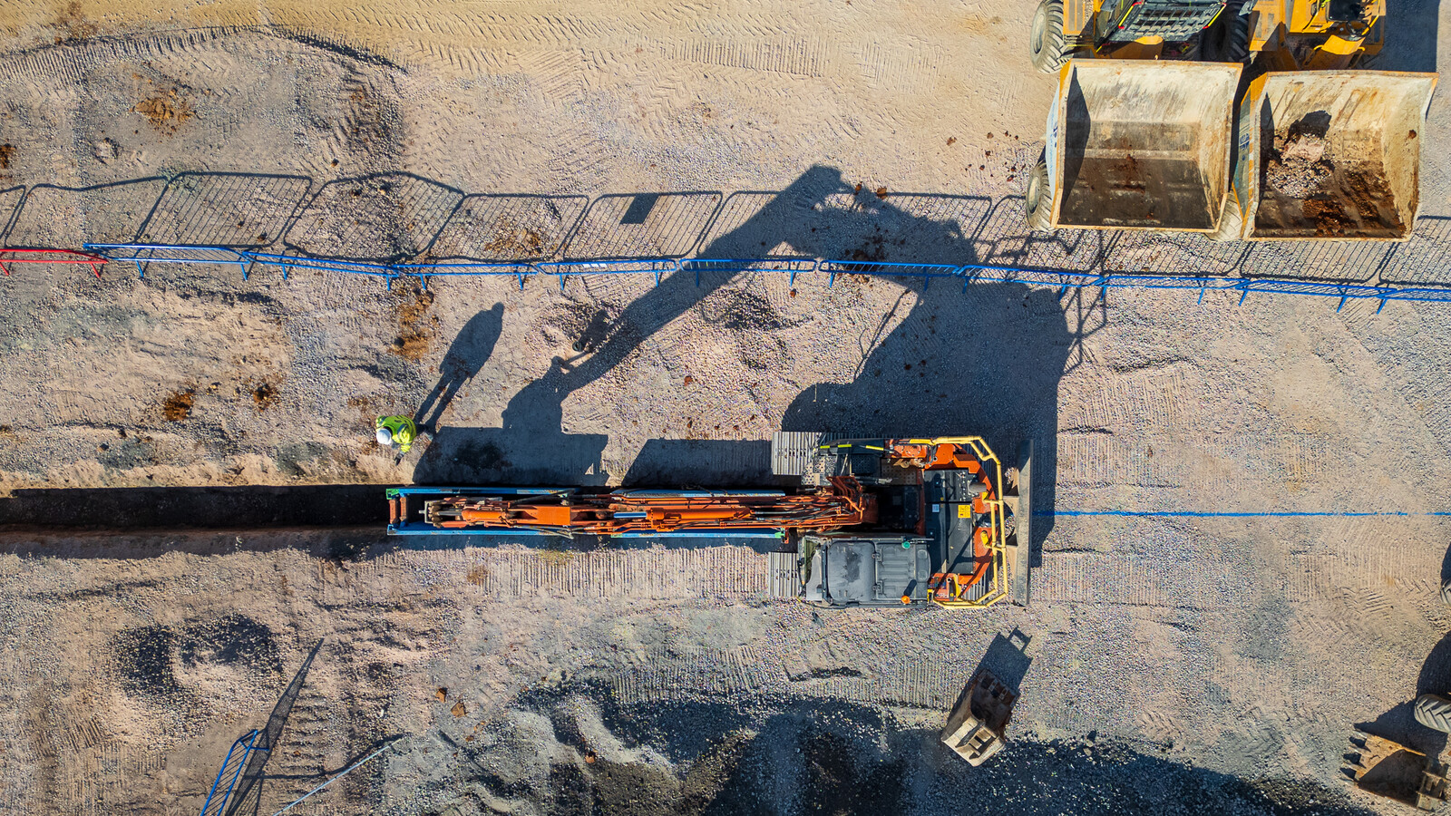 Drone shot of excavator installing deep sewer drainage top down with shadows