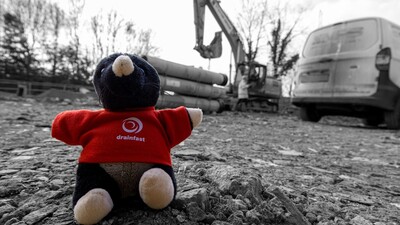 A cuddly mole toy wearing a Drainfast t-shirt sat in a building site.
